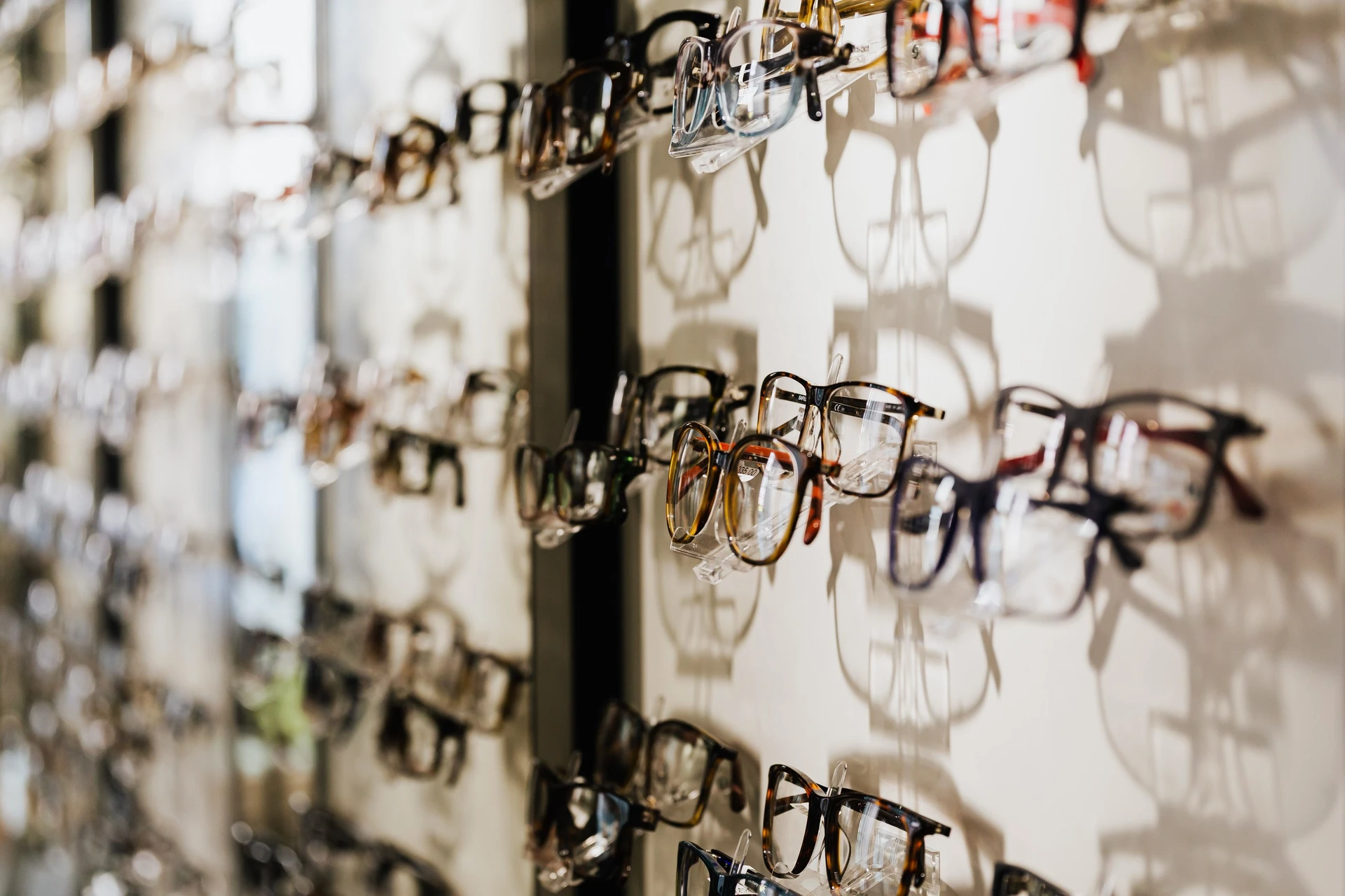Glasögonbågar uppställda på rad längs en ljus vägg i en optikbutik